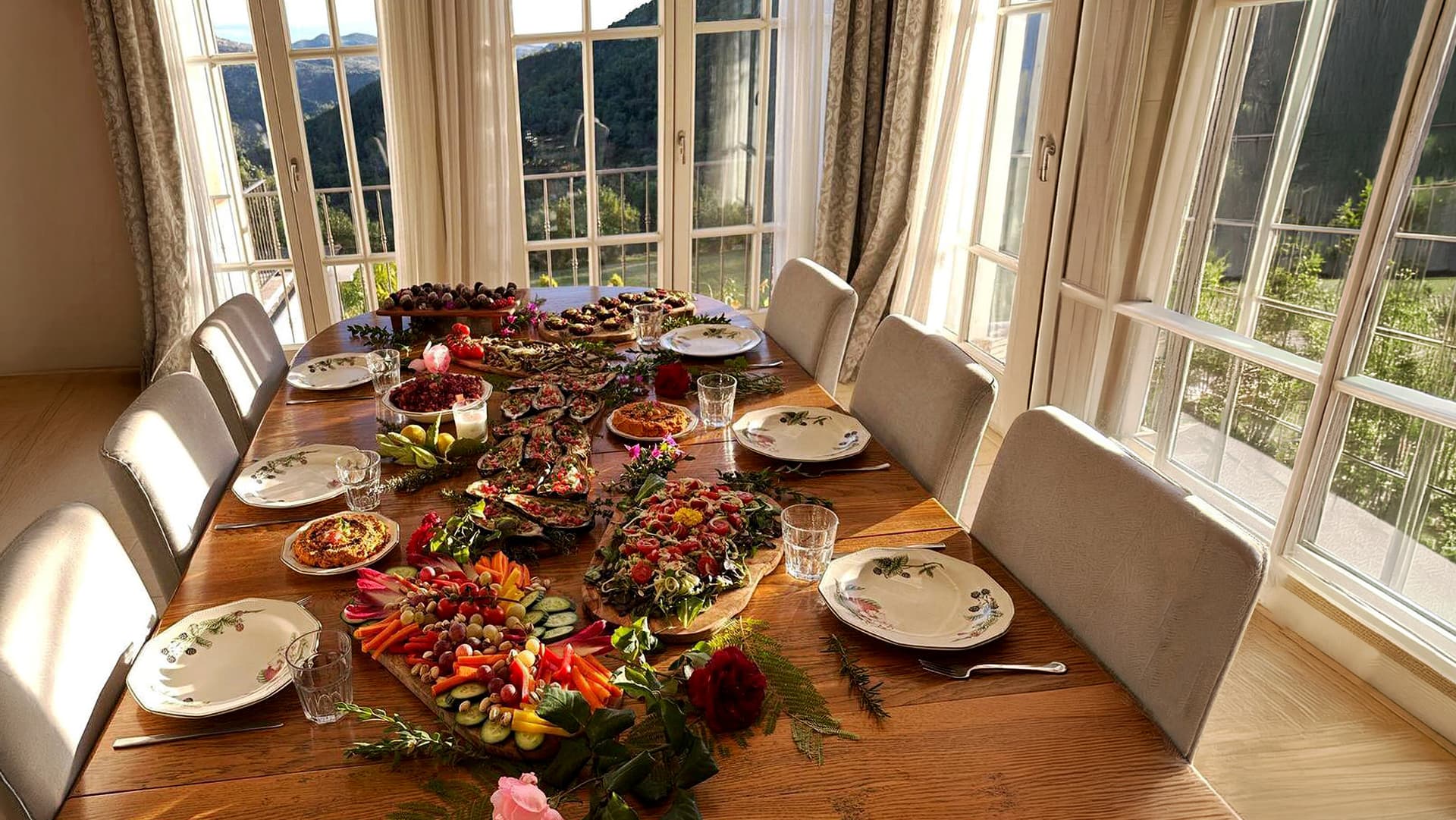 A sunlit retreat table filled with colourful dishes beside windows overlooking the mountains